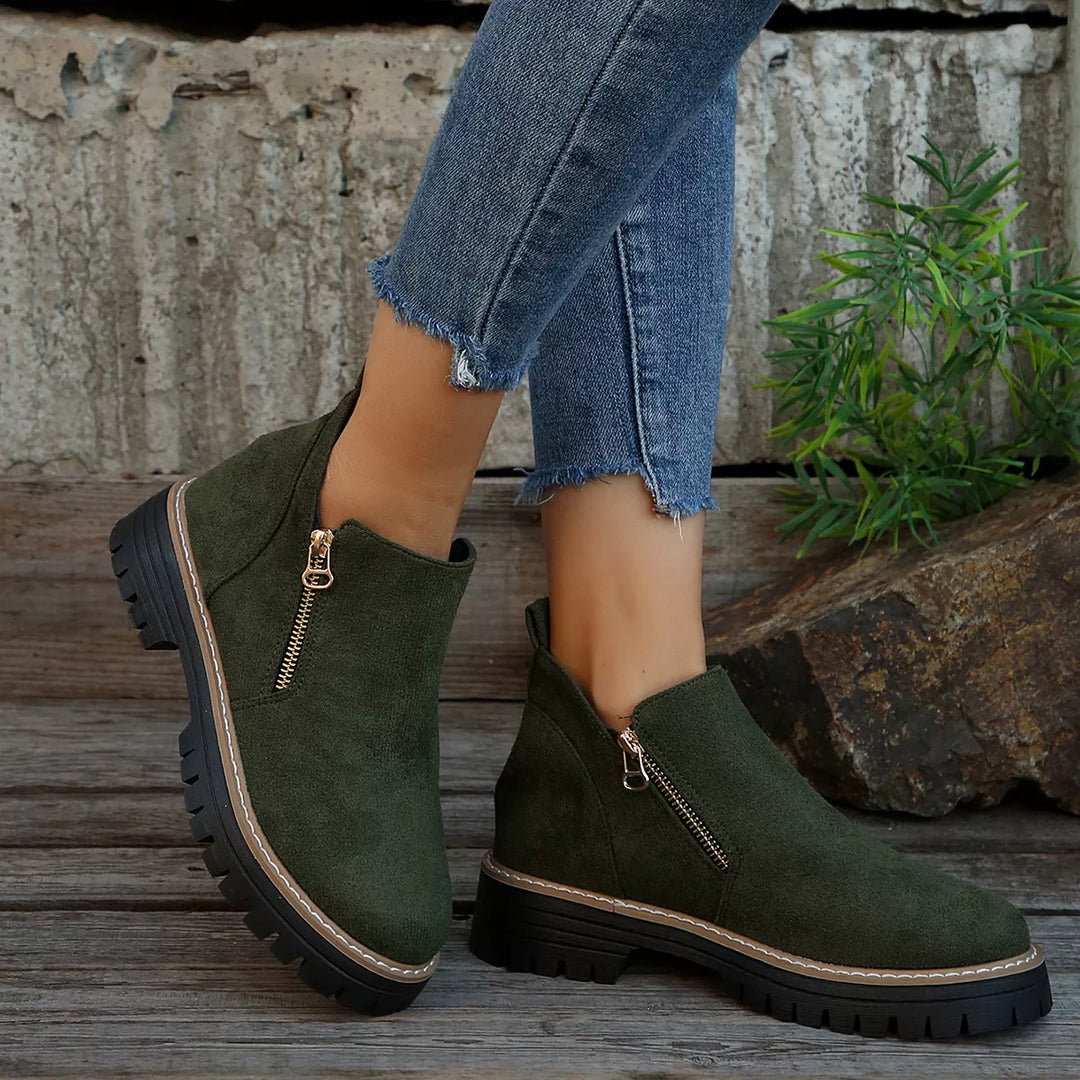 Women's ankle boots in olive green with chunky lug sole and side zipper, worn with jeans