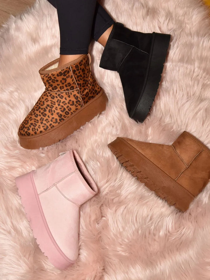 Leopard print platform slip on boots laid on a fuzzy rug beside other colors
