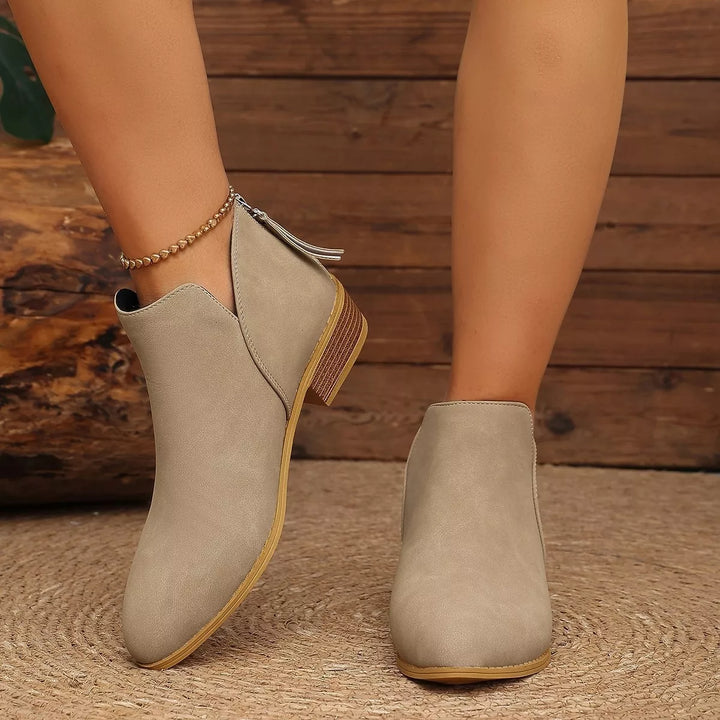 Taupe V-cut ankle boots with a low block heel, side view on a rug