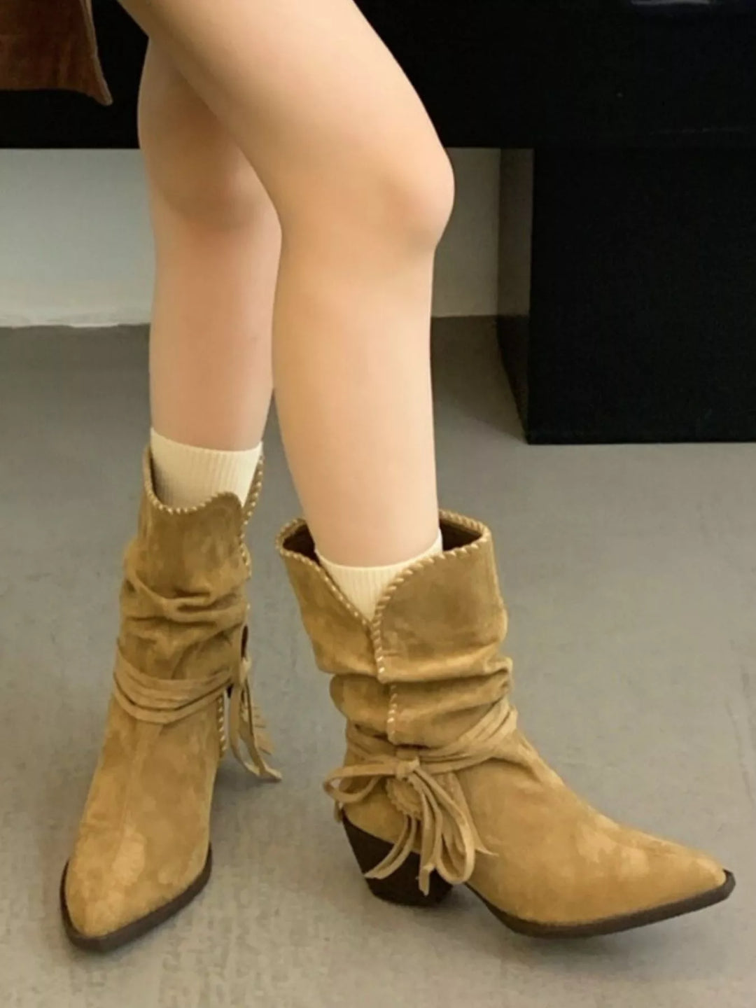 Pair of tan block heel ankle boots with fringe tie worn with cream socks