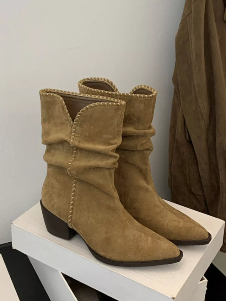 Women's ankle boots in tan with slouchy block heel and fringe tie, displayed on a stand