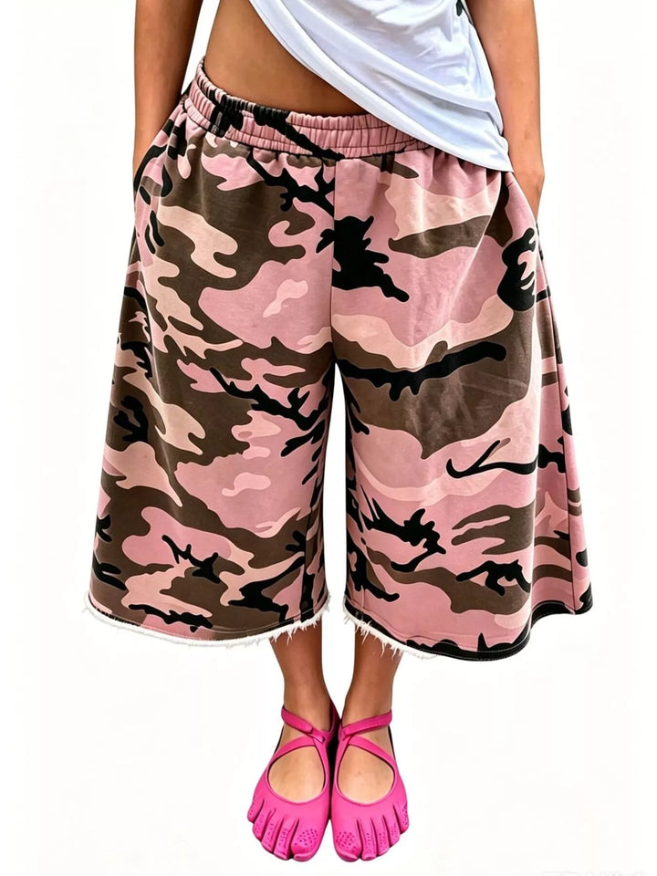 Pink camo knee length baggy shorts with a frayed hem, studio shot