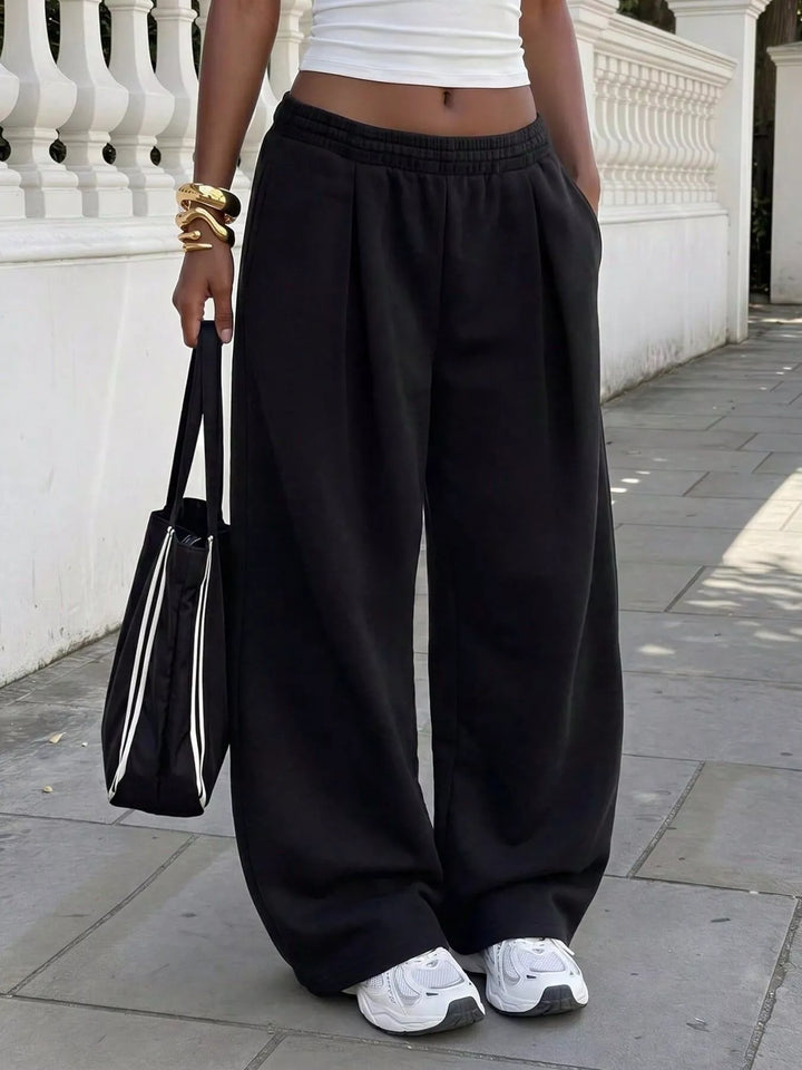 Black baggy sweatpants with pleated front, carried with a tote bag