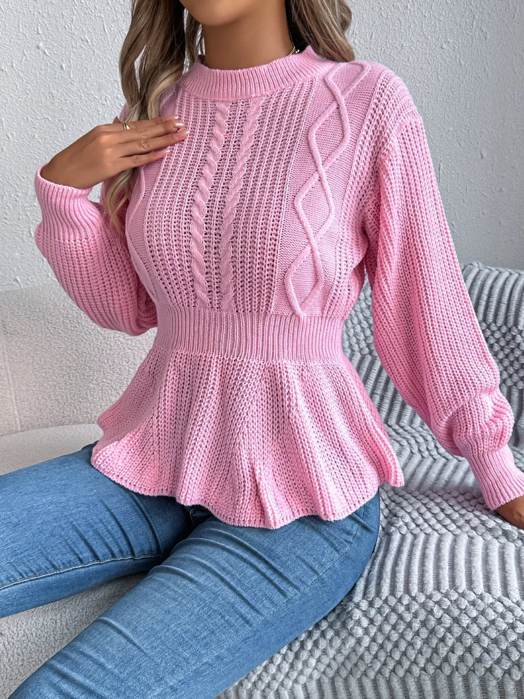 Pink cable knit sweater seated pose with arm resting on the knee