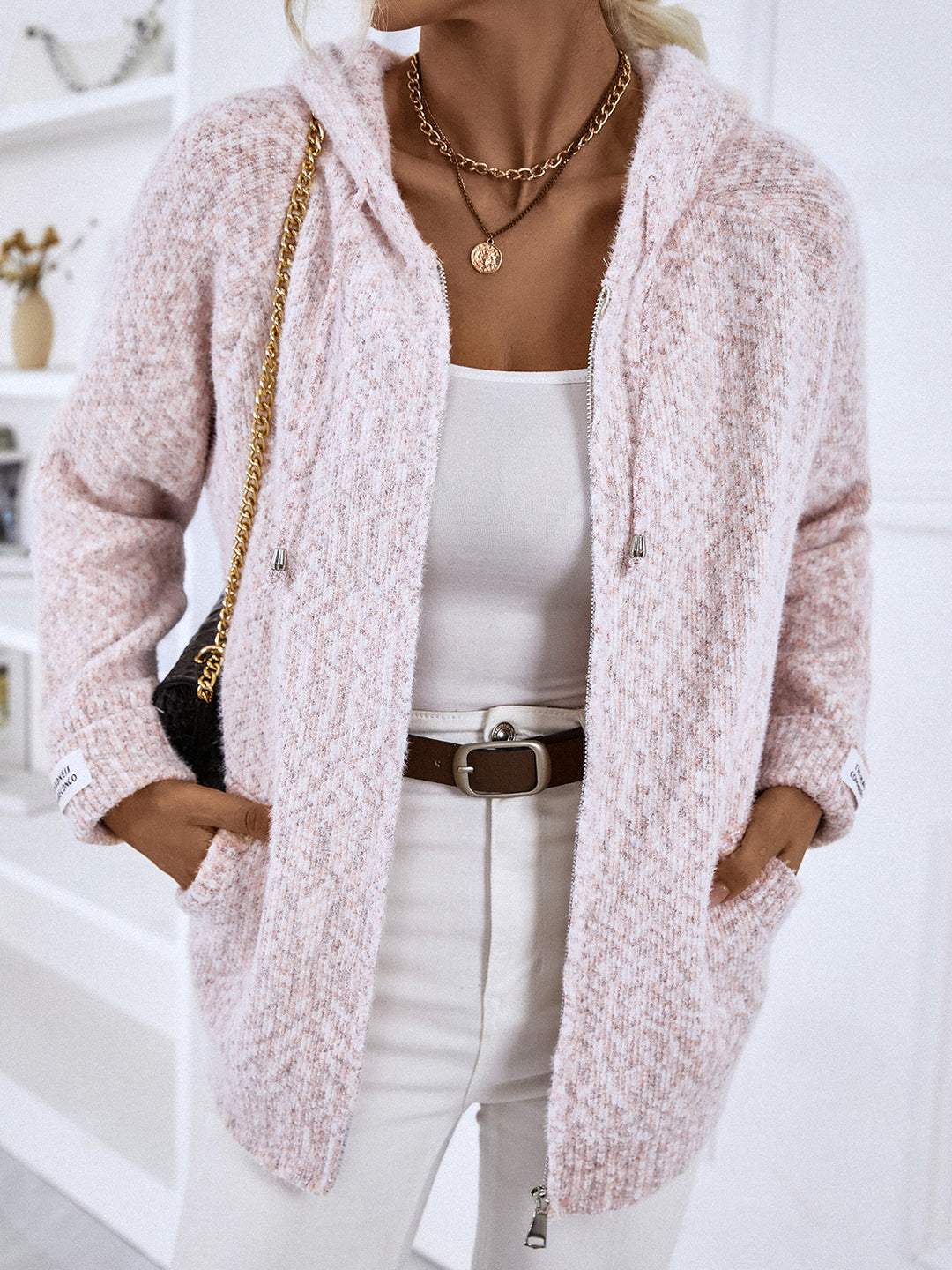 Blush pink hooded cardigan worn open with white pants and a shoulder bag
