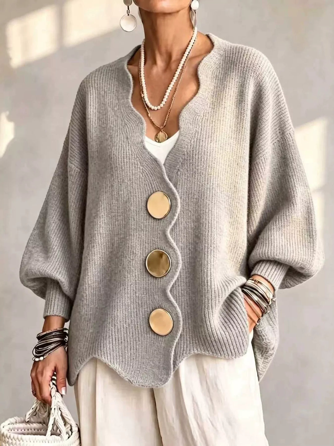 Oversized scalloped edge cardigan in light gray with gold buttons, worn over white pants