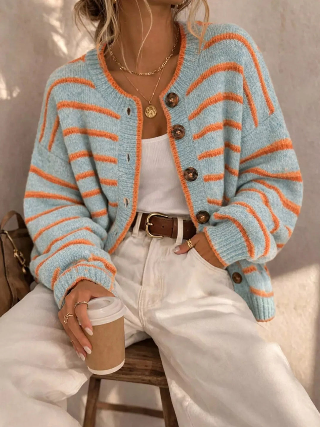 Light blue striped cardigan styled with white jeans, seated on a wooden stool
