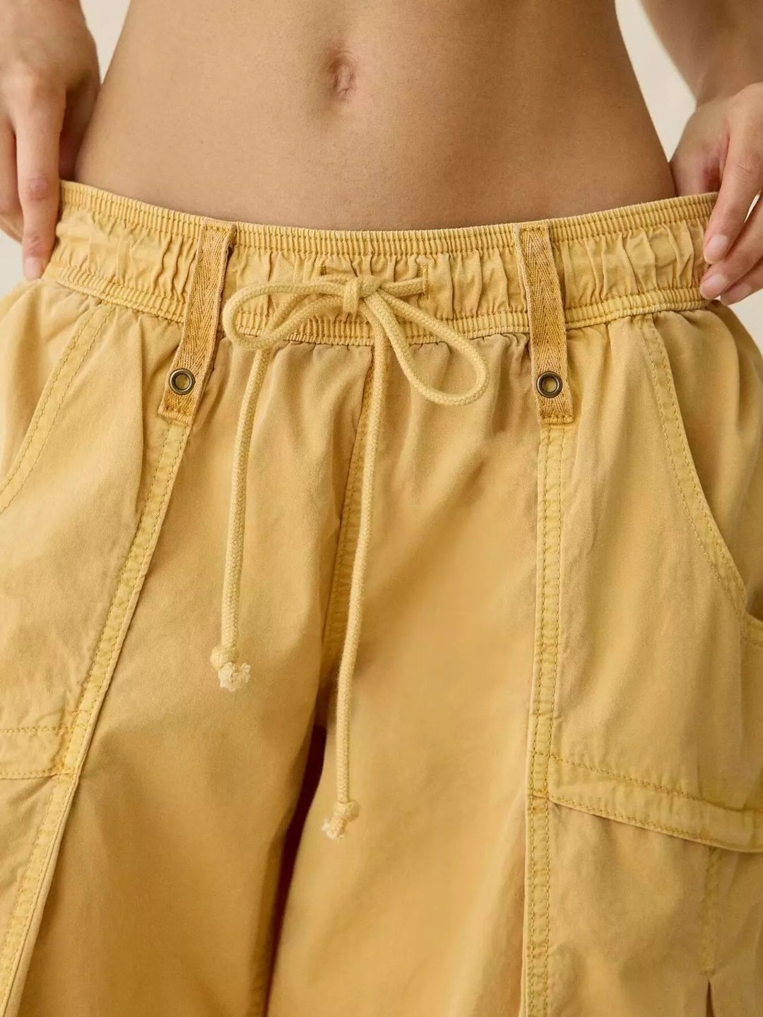 Close-up of mustard cargo pants drawstring waistband and pockets