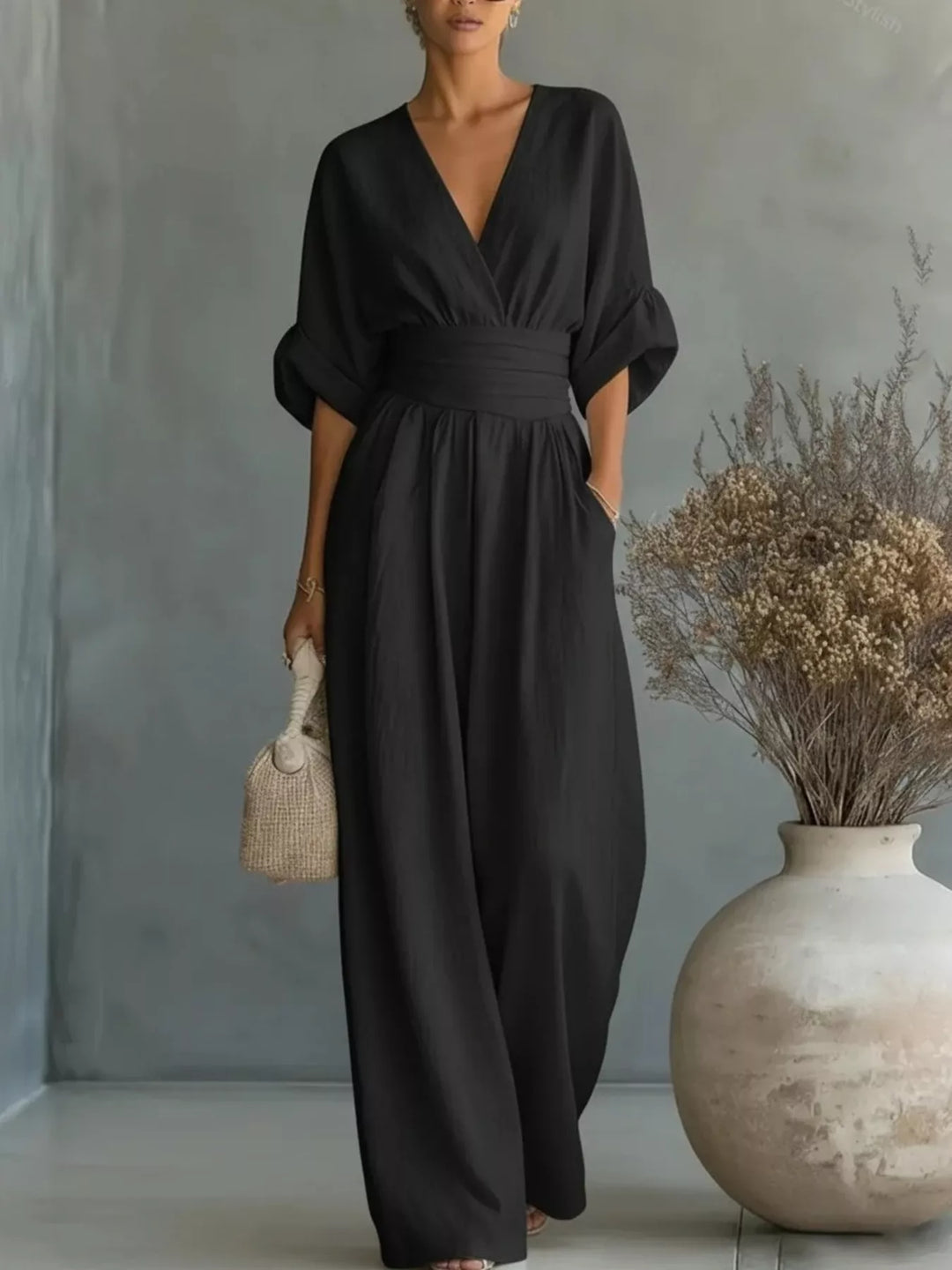 Black deep V neck wrap jumpsuit with half sleeves, standing by a vase