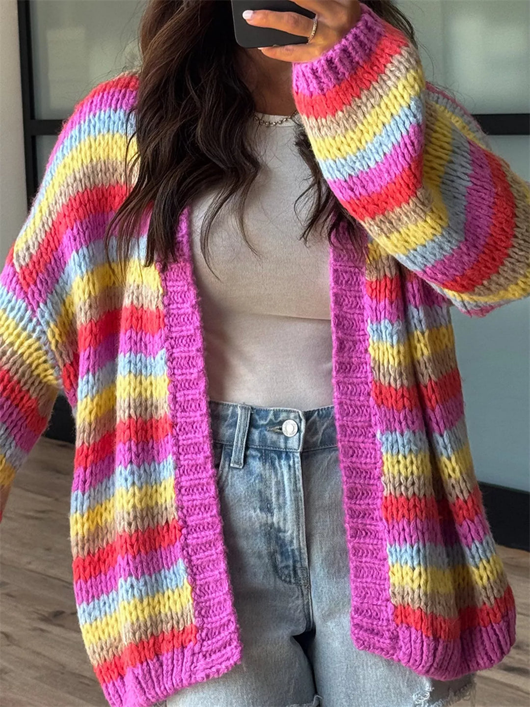 Women's chunky knit cardigan in rainbow stripe, oversized open front, worn with denim shorts