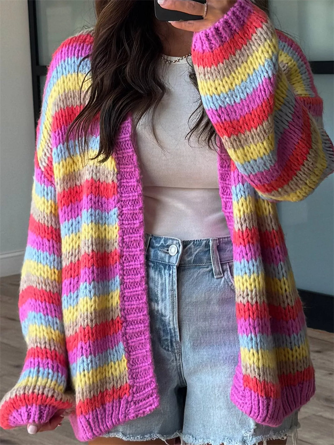 Rainbow stripe chunky knit cardigan worn open over a white tank and cutoff shorts