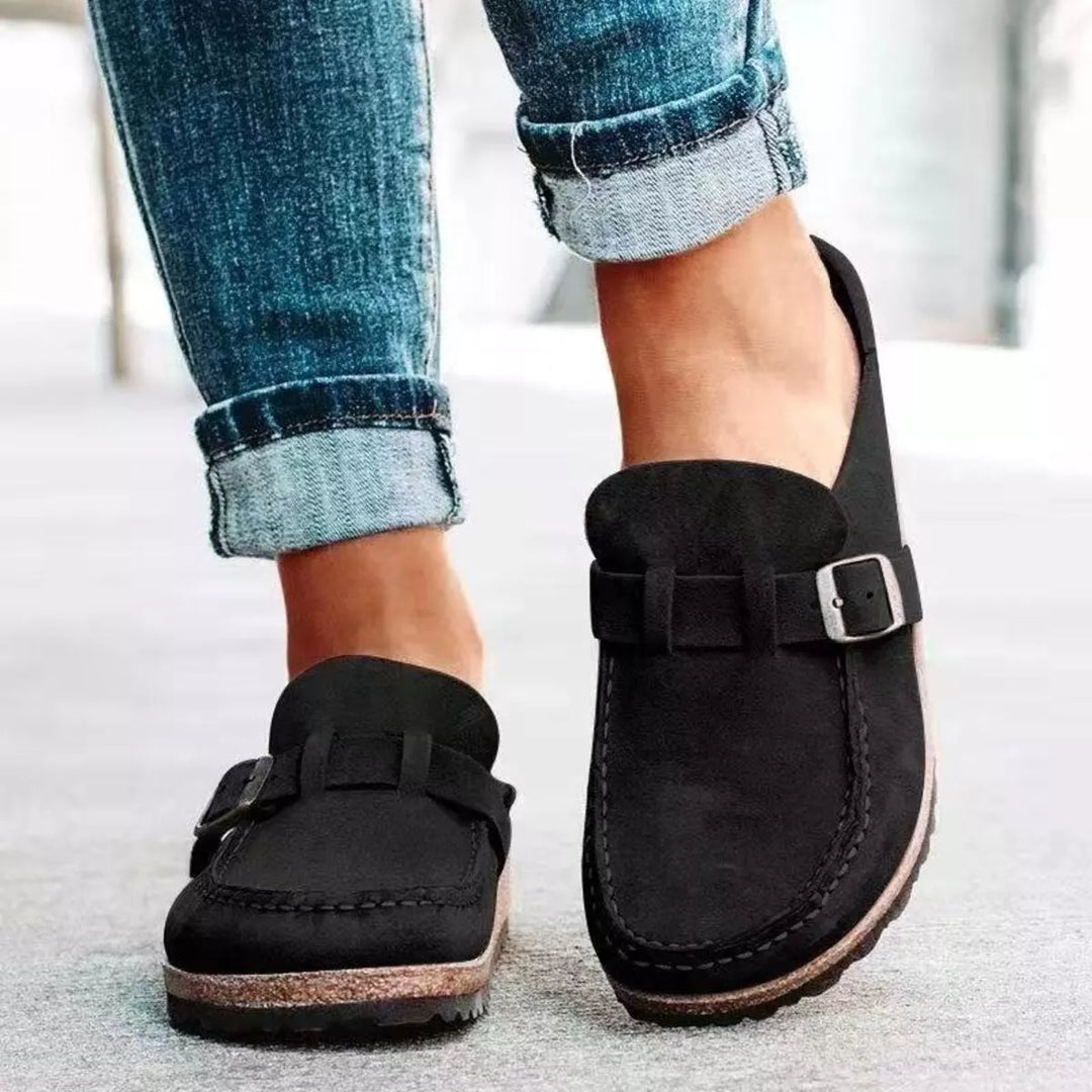 Black slip on clogs with buckle strap worn with cuffed jeans, front view