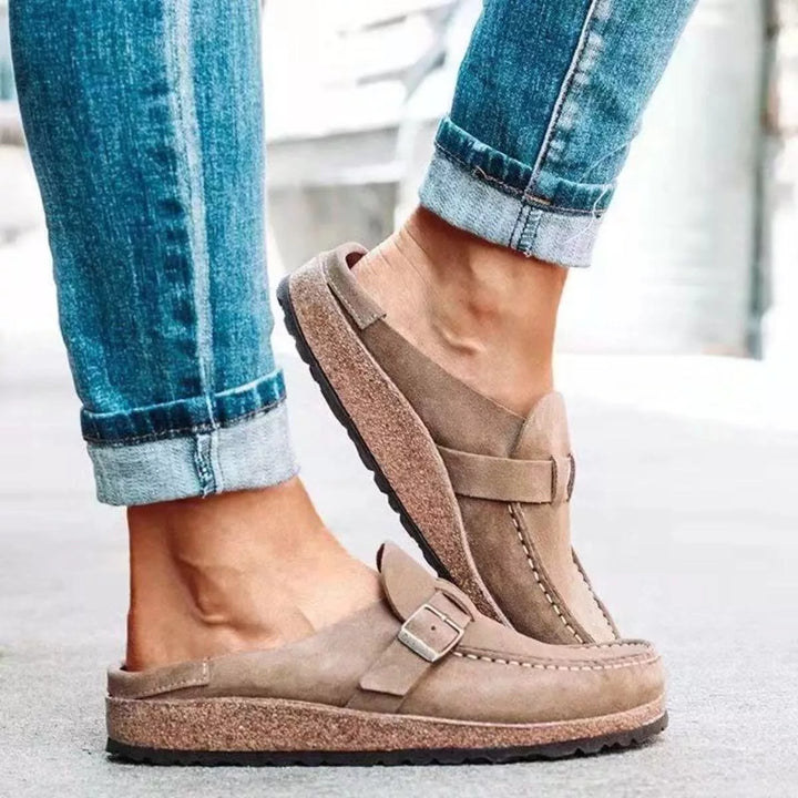 Taupe clog worn mid step, showing the buckle strap and cork-look footbed