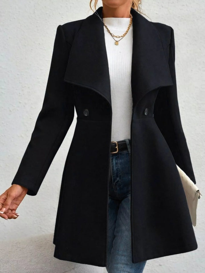 Black fit and flare coat worn open over a white top and jeans