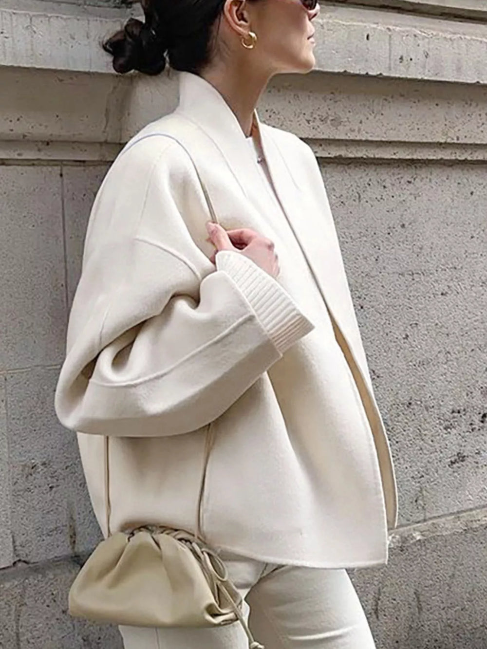 Side view of ivory open front cropped jacket worn with a clutch