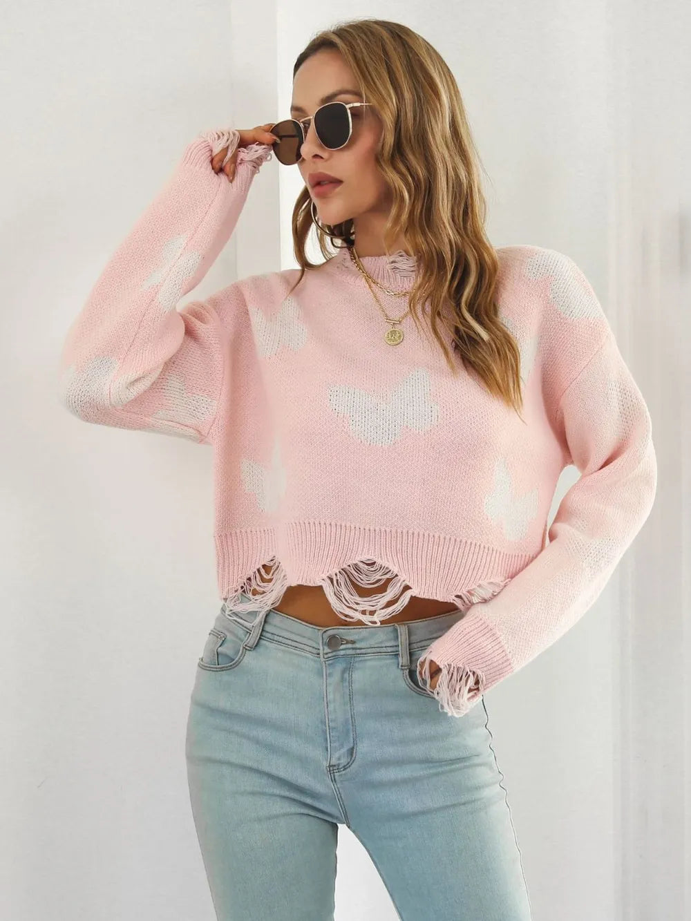 Blush pink cropped sweater with hand raised to sunglasses