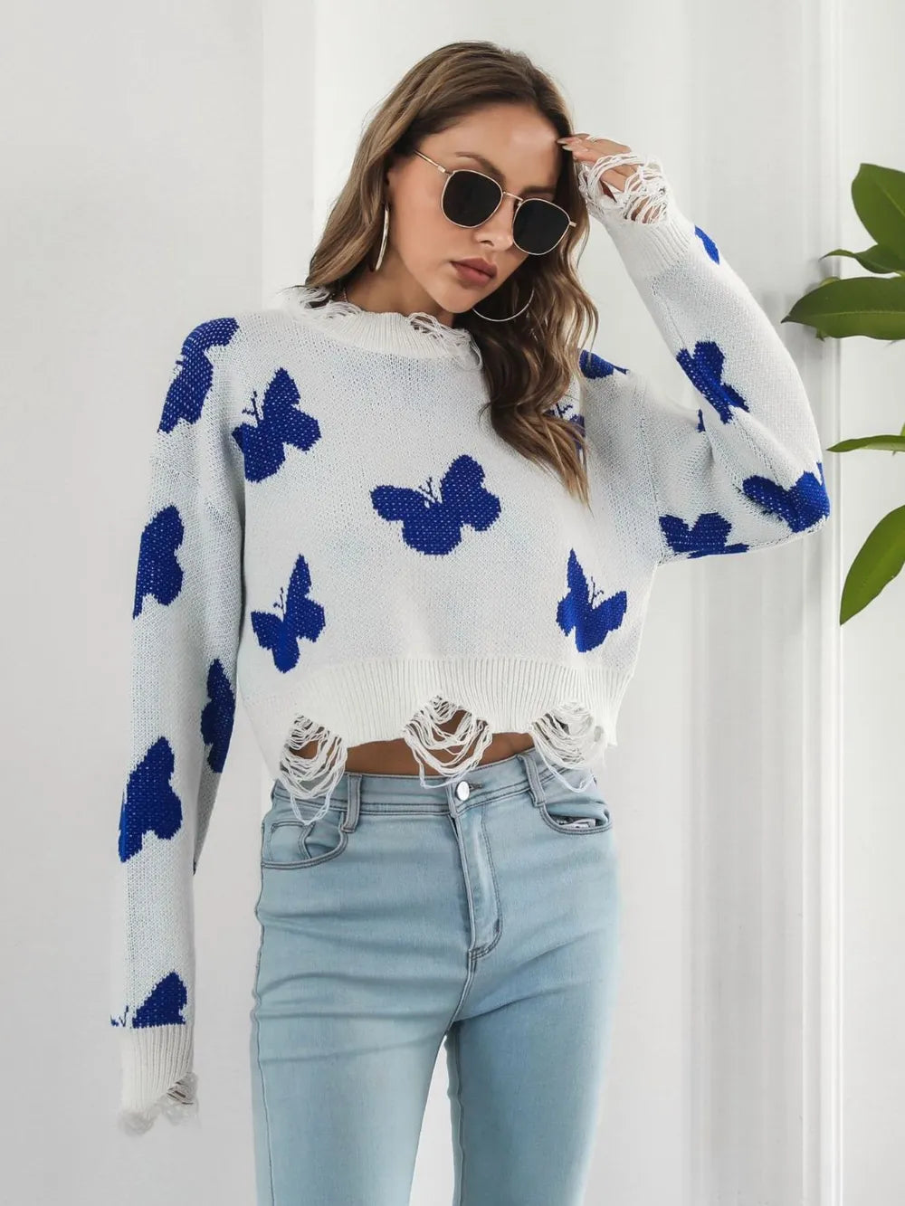 White butterfly sweater with hand raised to sunglasses, three quarter view