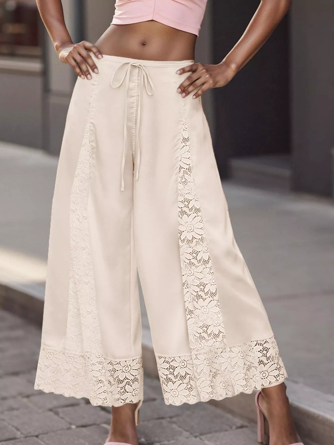 Close-up of the ivory pants lace panel and scalloped lace hem against a street backdrop