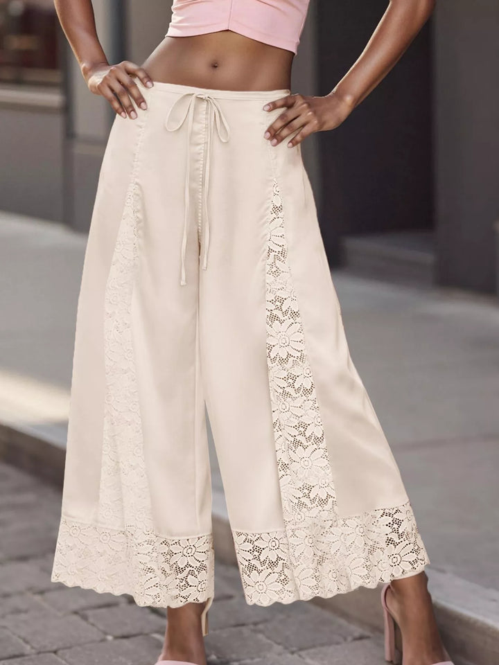 Close-up of the ivory pants lace panel and scalloped lace hem against a street backdrop