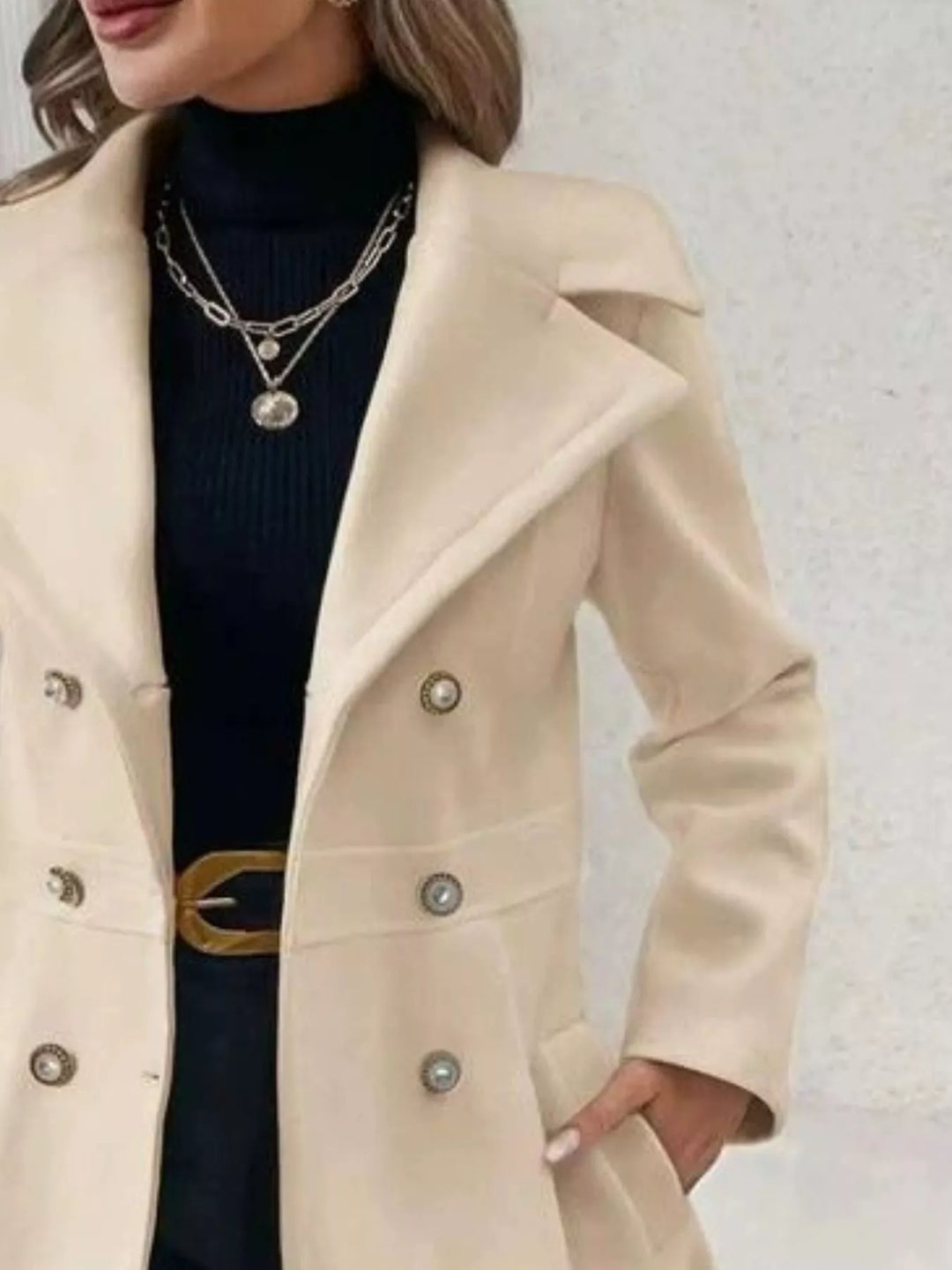 Close-up of the beige coat lapel, gold buttons and belt detail