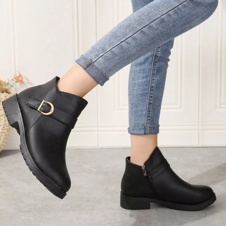 Black low block heel boots seen from the side with buckle detail while stepping