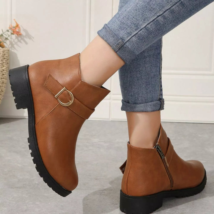 Cognac ankle boots with buckle worn mid stride, heel and sole visible
