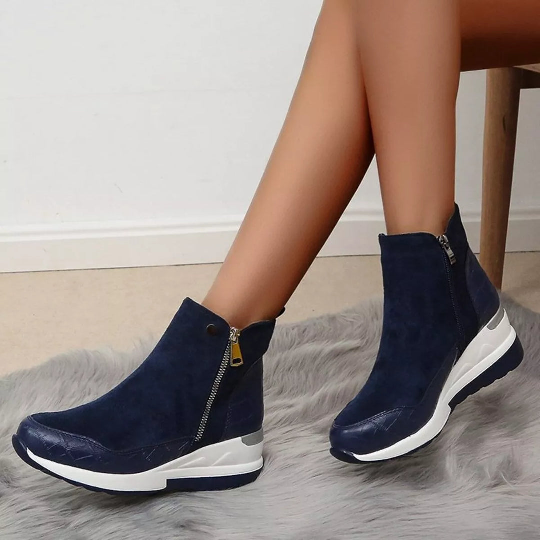 Navy platform wedge boots worn with crossed legs against a white wall