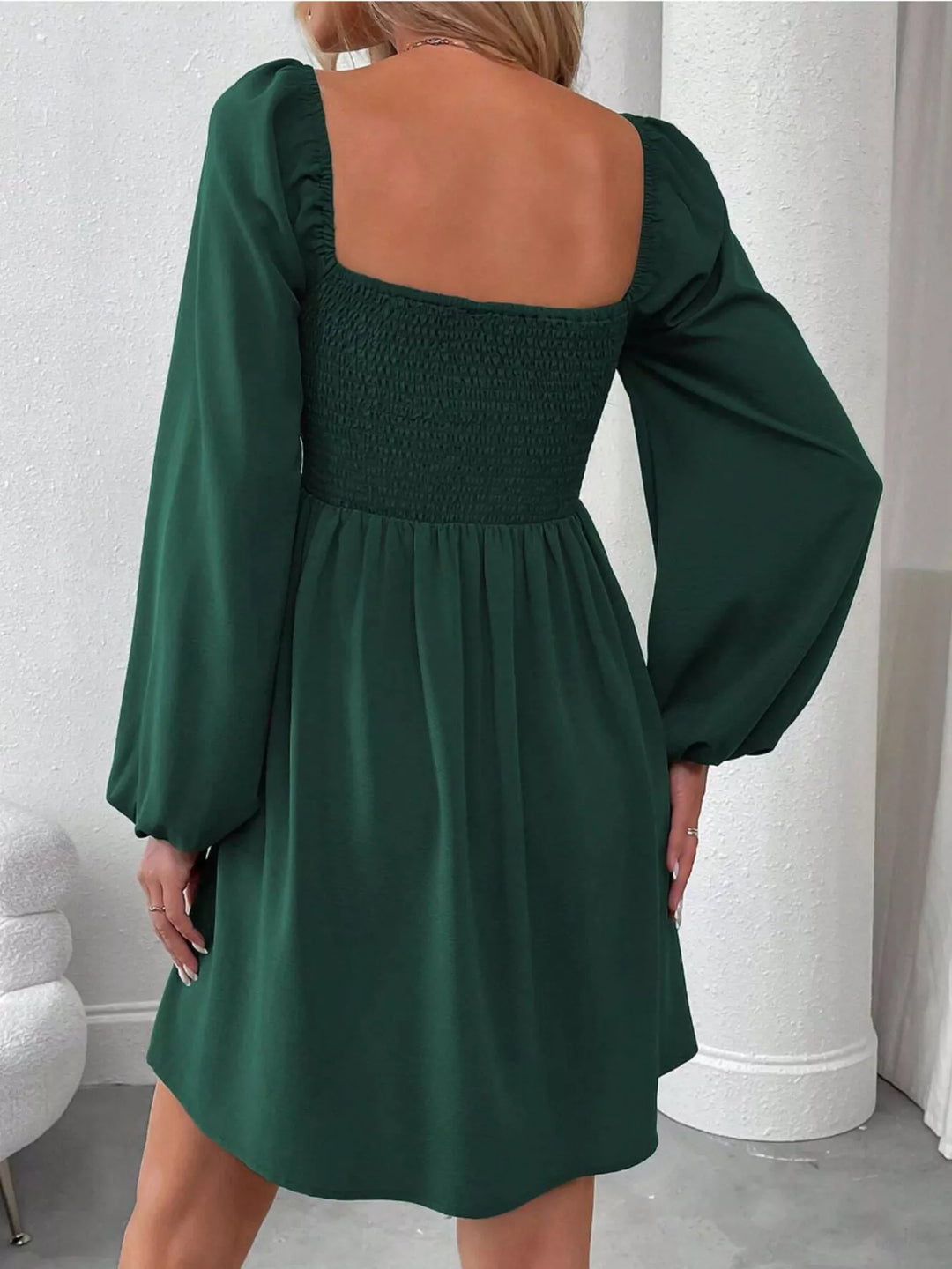 Dark green mini dress worn on a model, showing the ruched smocked bodice