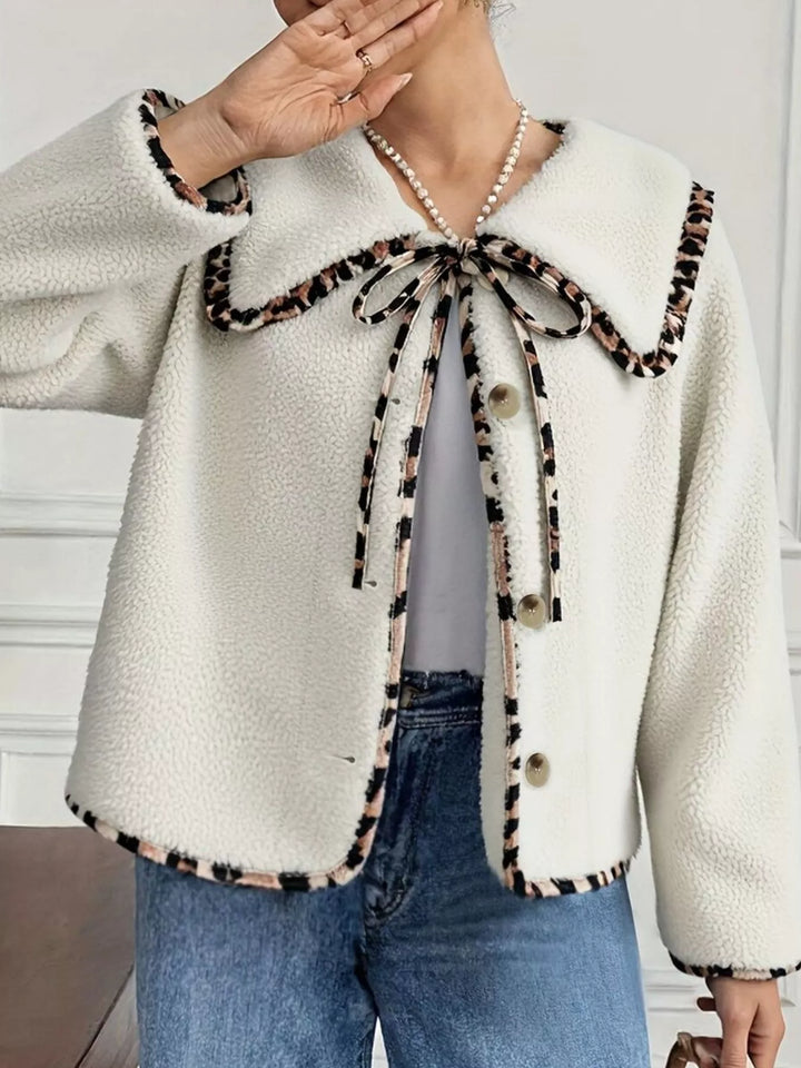 Cream fall jacket with leopard print bow tie and button front, hand near the face