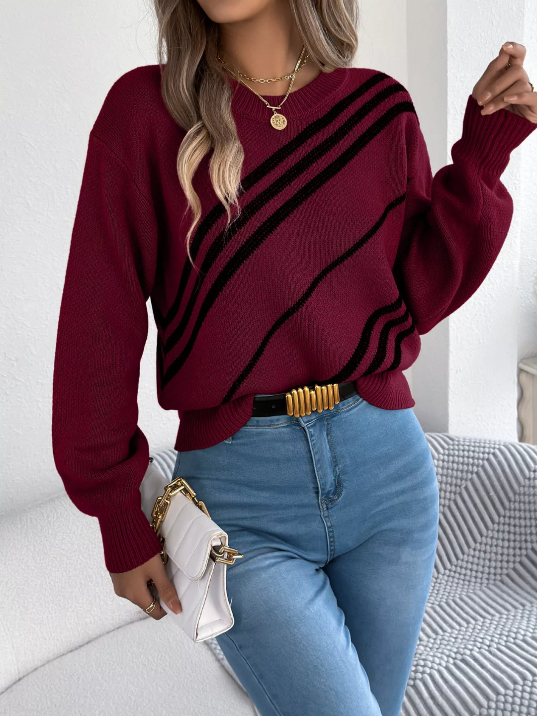 Burgundy crew neck sweater with bold black diagonal stripes, holding a clutch