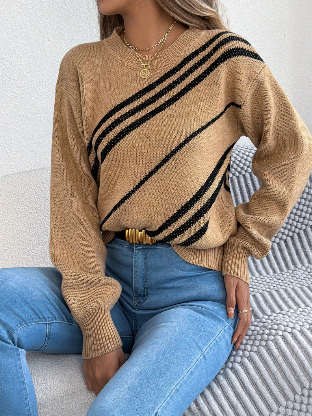 Camel diagonal stripe sweater seated on a couch with jeans and a belt