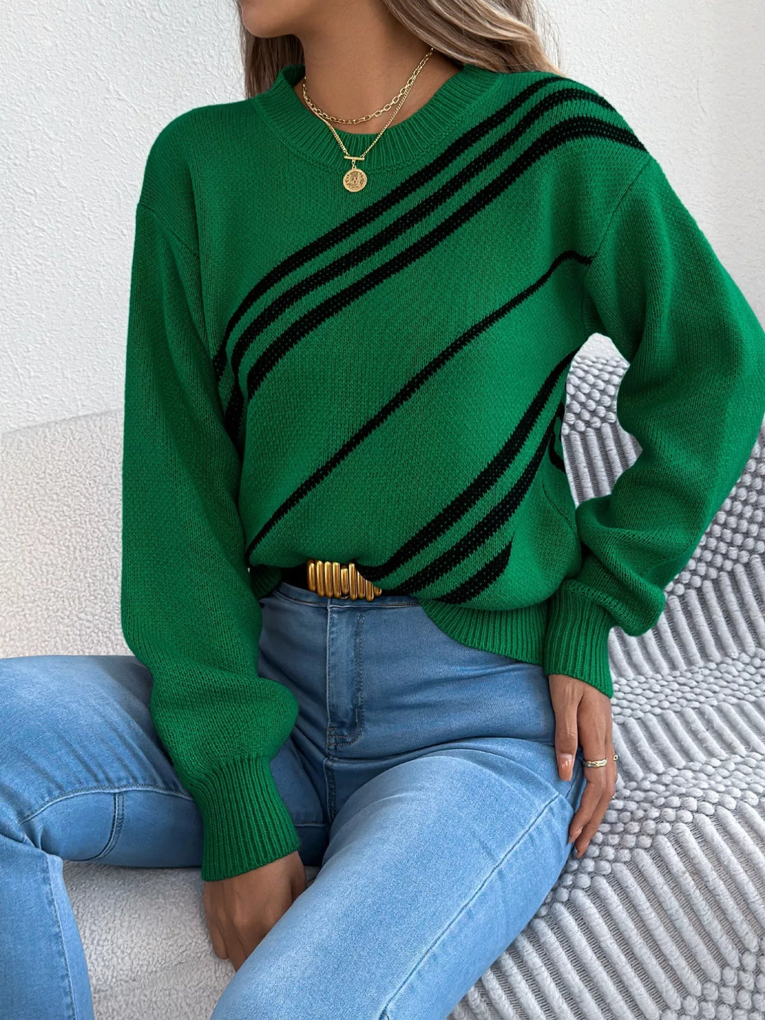 Emerald striped sweater seated on the couch with a gold belt and jeans