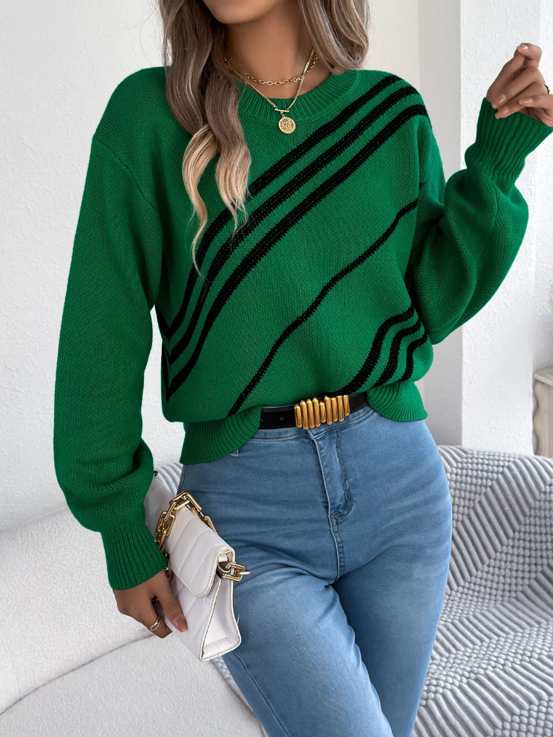 Emerald crew neck sweater with a white clutch, hand lifted to the hair