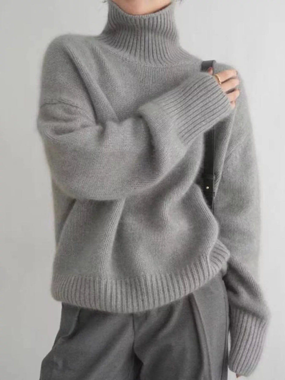 Gray turtleneck sweater shown at an angle with a black shoulder strap