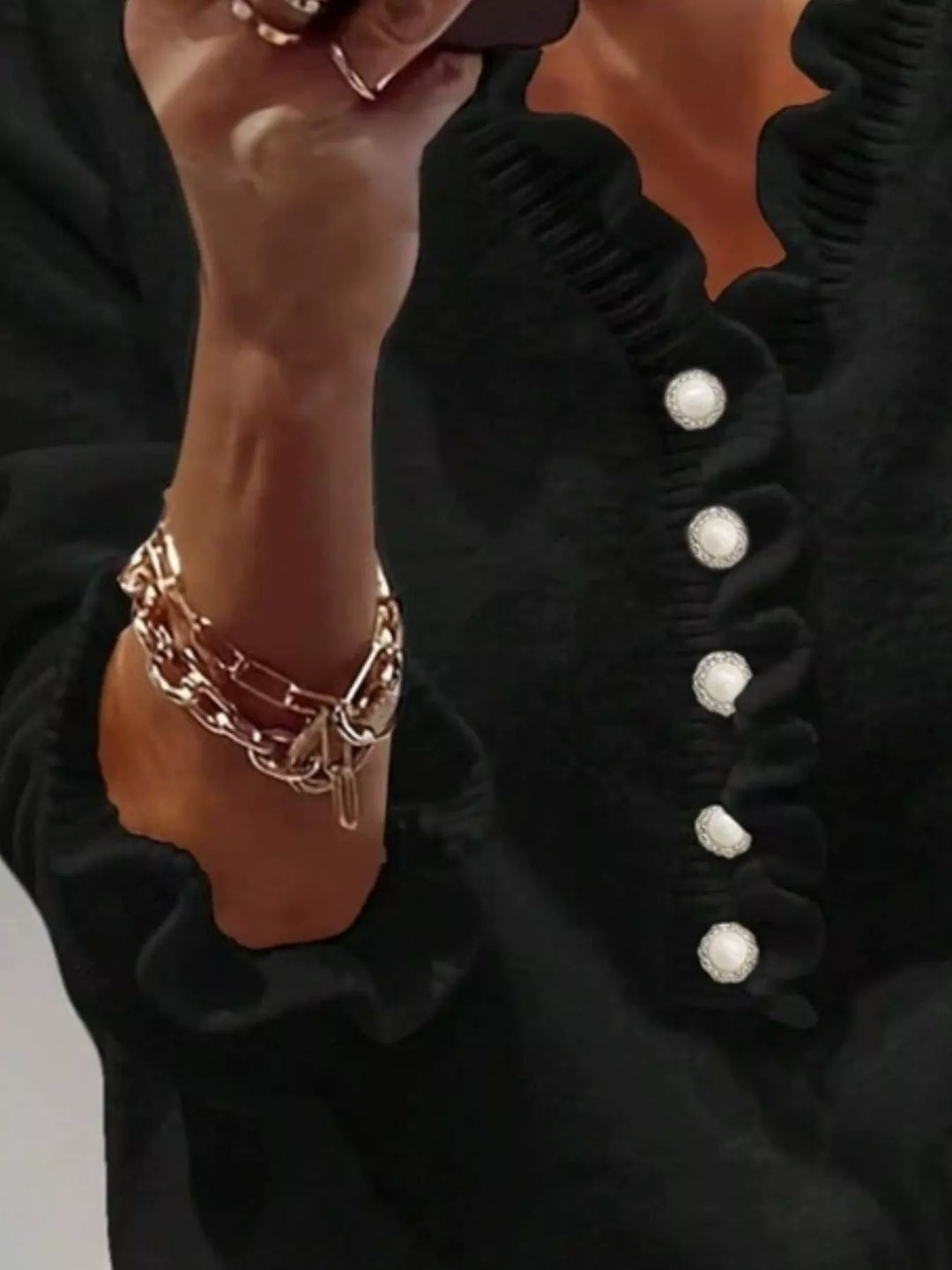 Black sweater button placket and ruffle trim, seen with a chain bracelet