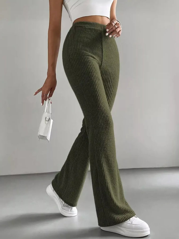 Women's flare pants in olive green, high waisted ribbed look, walking pose with white sneakers