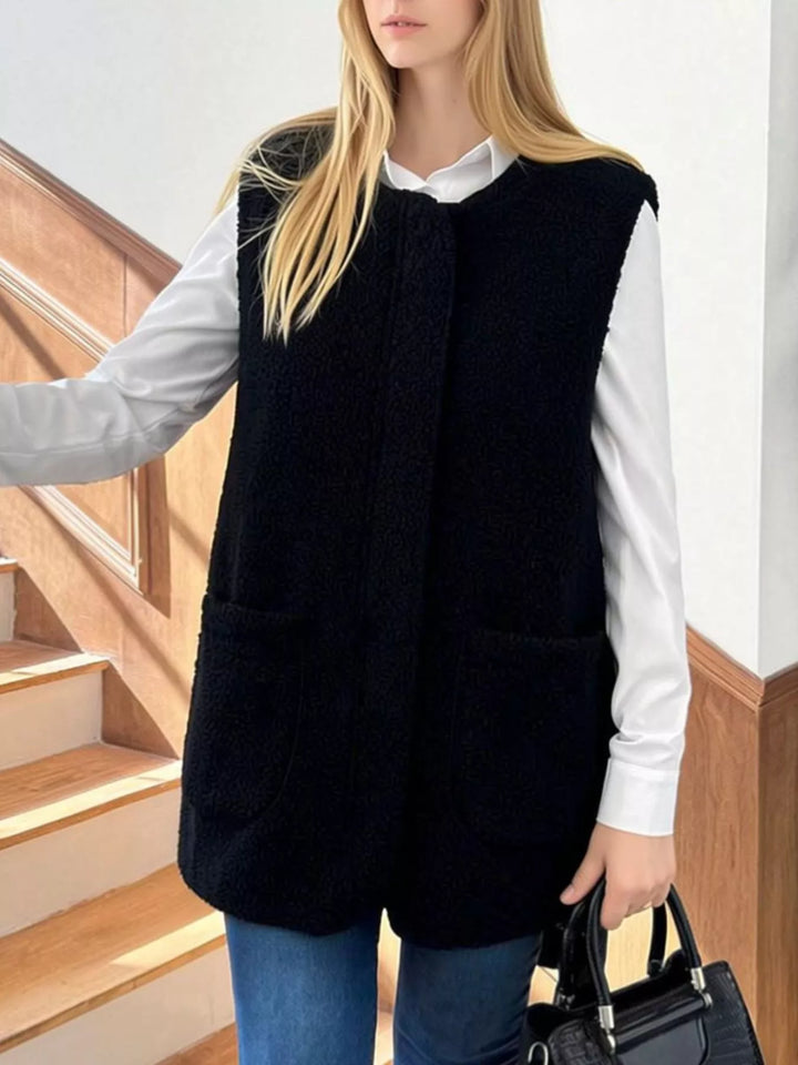Black fuzzy vest with a round neck and patch pockets, worn with jeans and a handbag