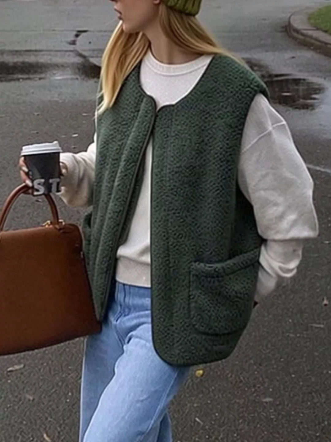 Forest green fuzzy vest worn open over a gray sweatshirt outdoors with a brown bag