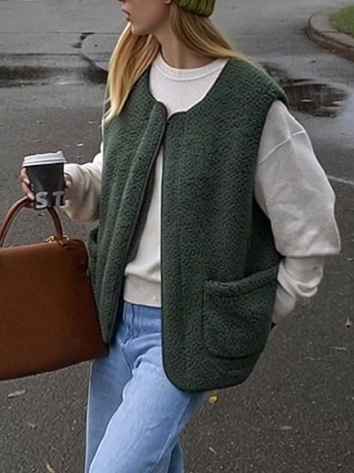 Forest green fuzzy vest worn open over a gray sweatshirt outdoors with a brown bag