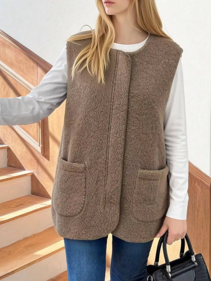 Taupe fuzzy vest with patch pockets and a curved hem, worn with jeans