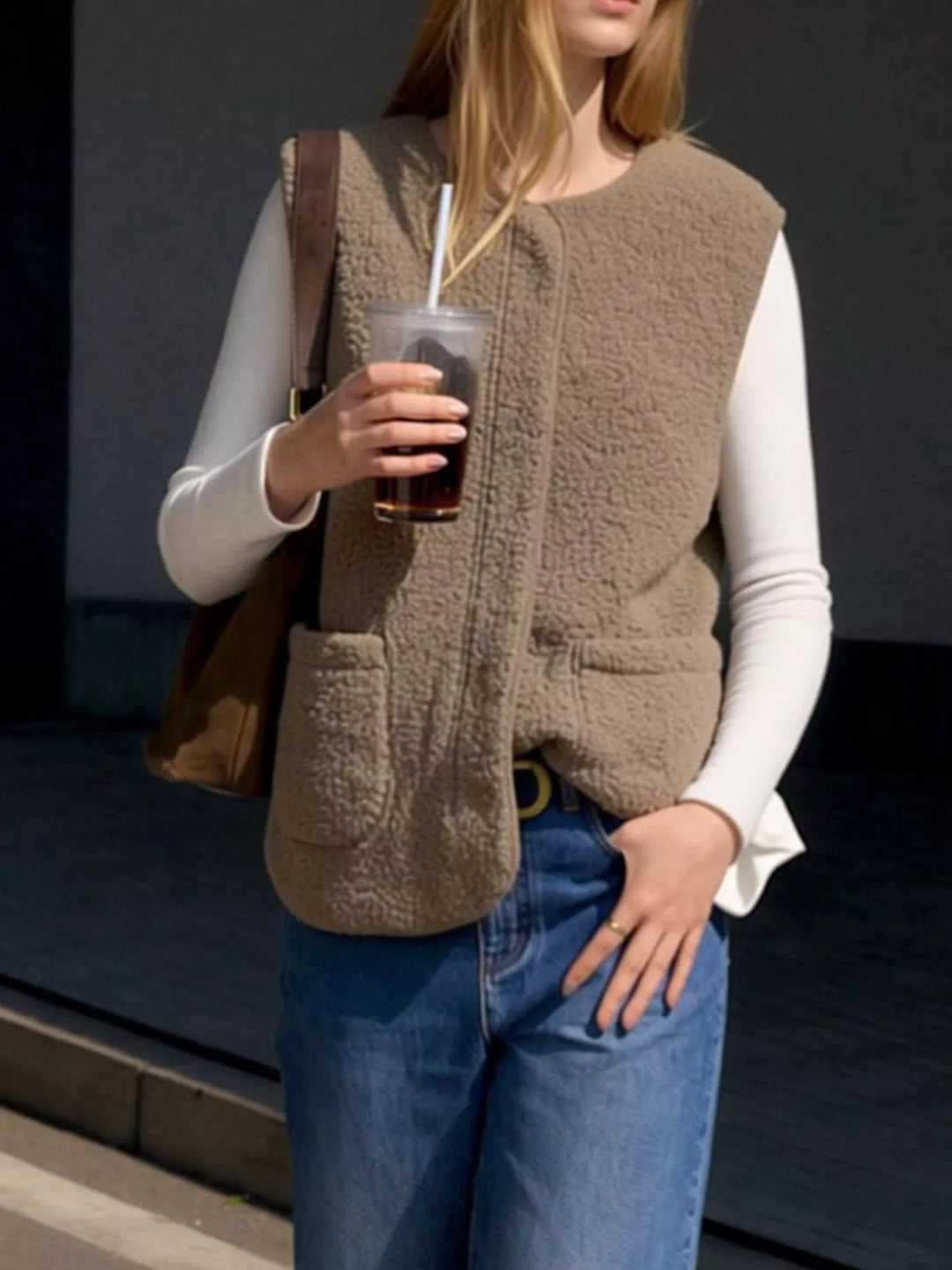 Taupe fuzzy vest styled with jeans and an iced drink against a dark background