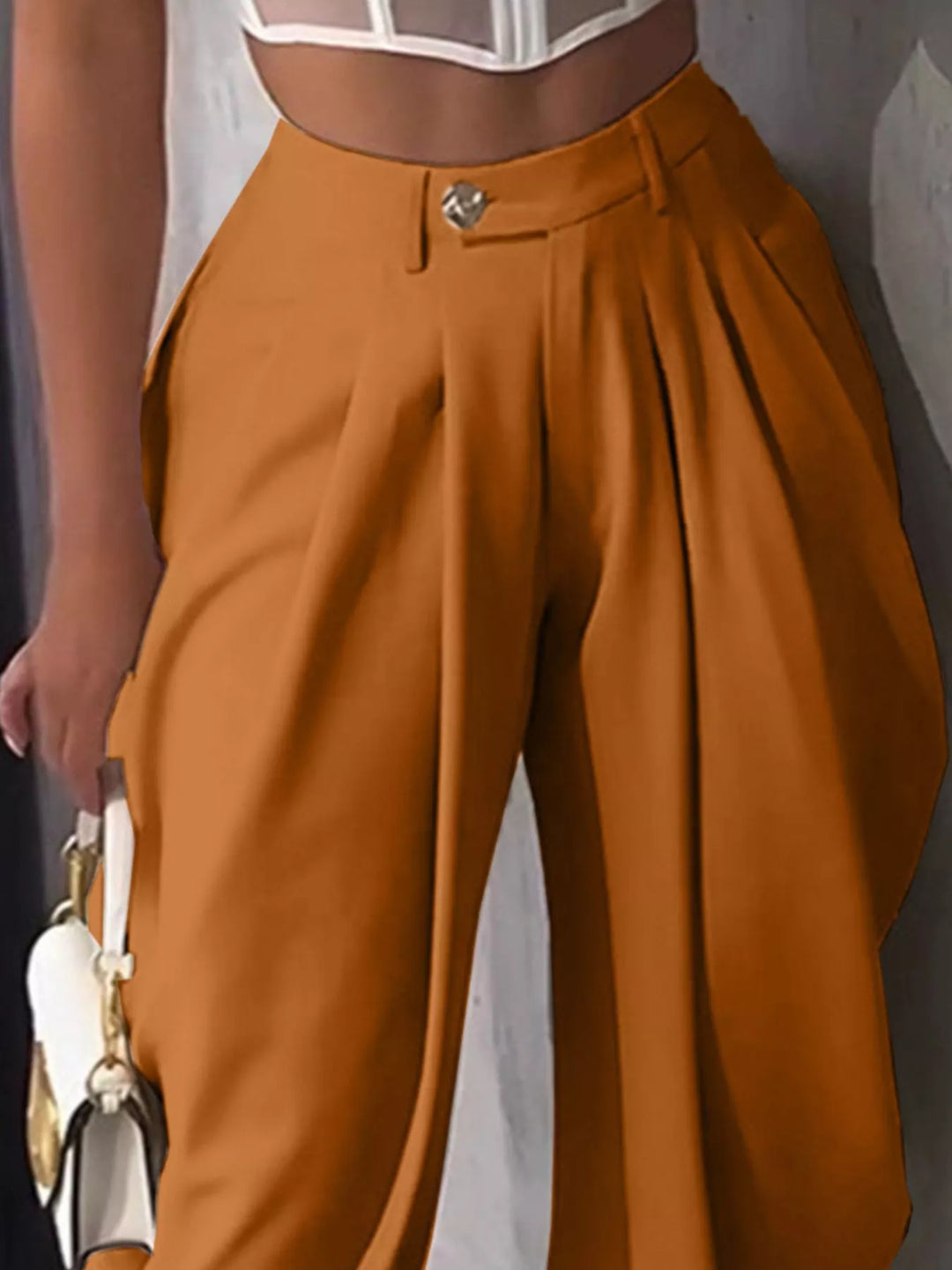 Close-up of burnt orange pleated harem pants with a gold button waist