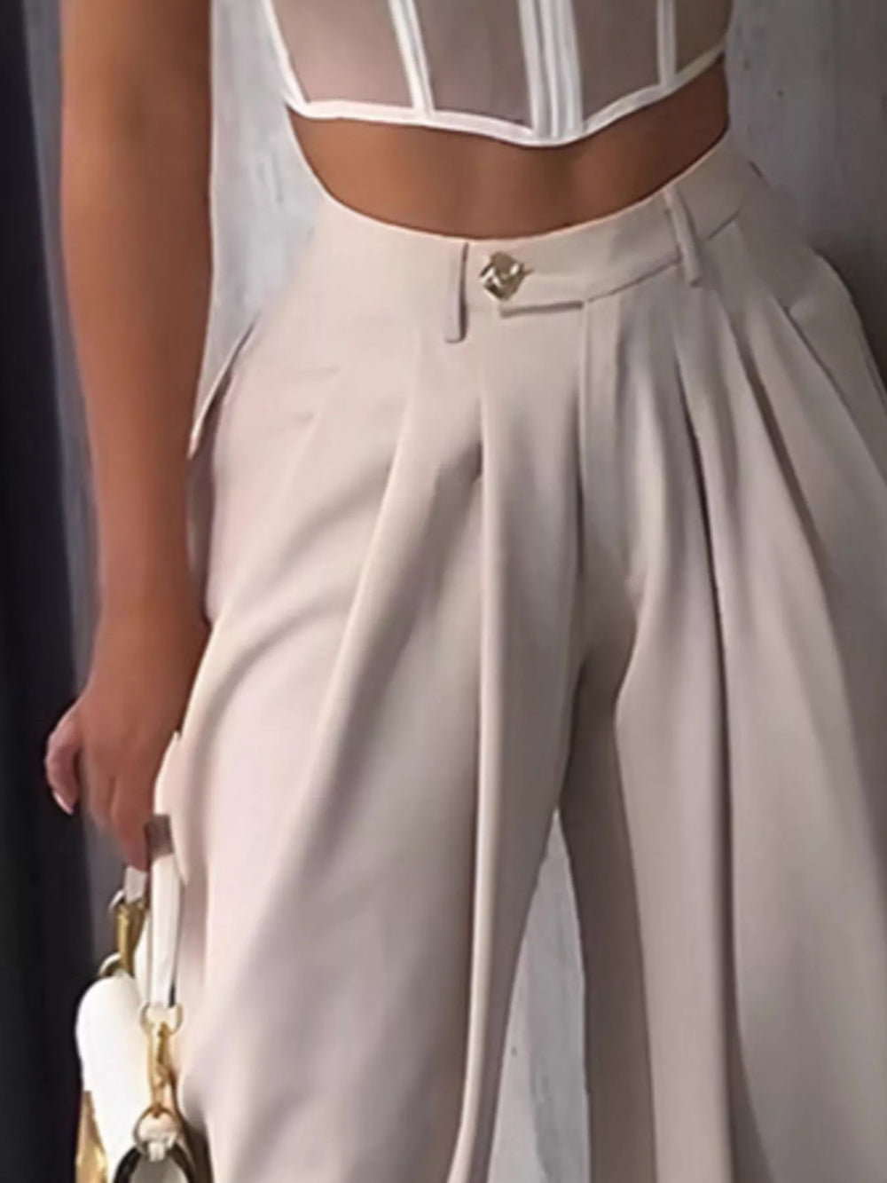 Close-up of the cream harem pants waistband with gold button and front pleats