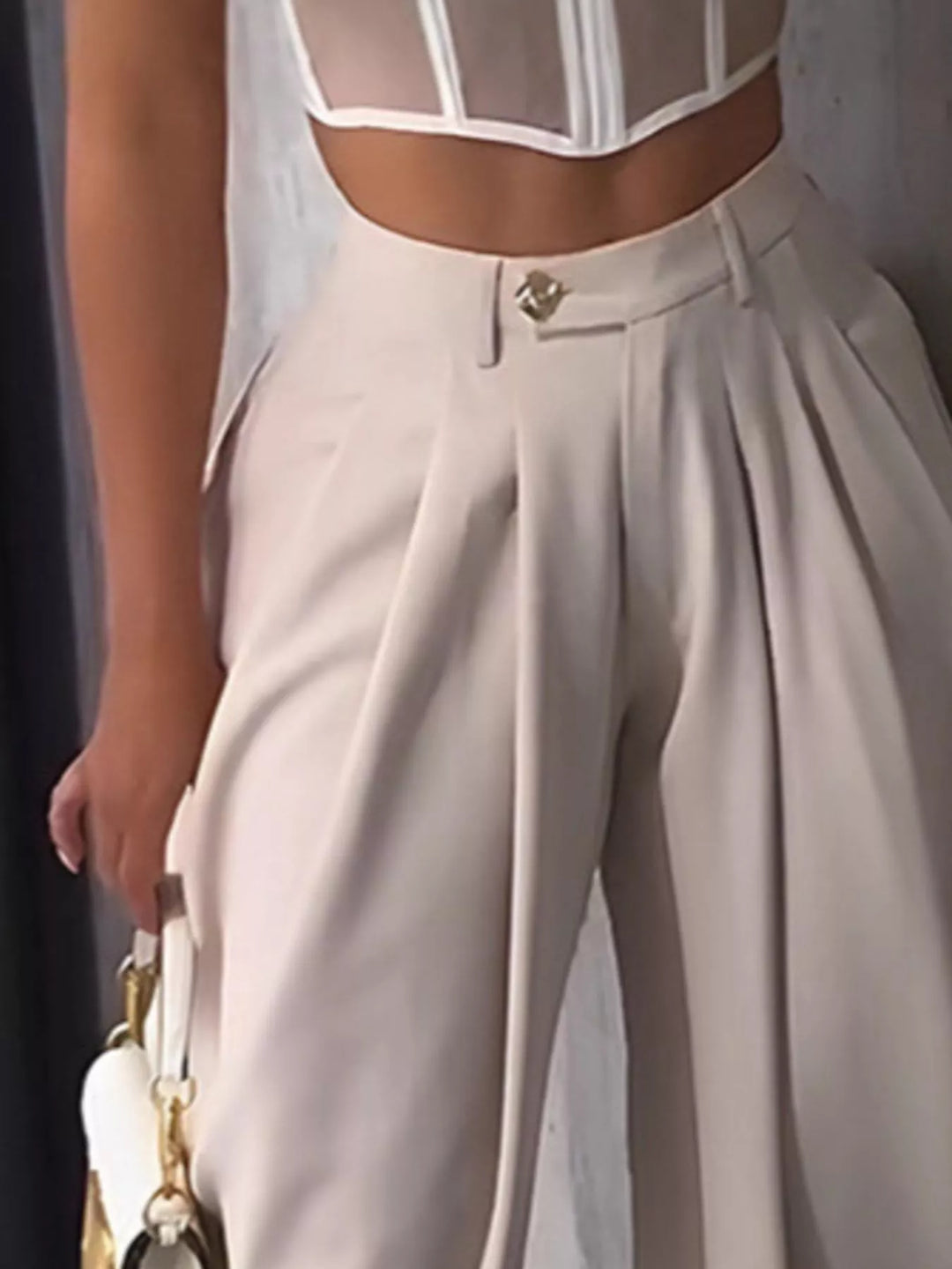 Close-up of the cream harem pants waistband with gold button and front pleats