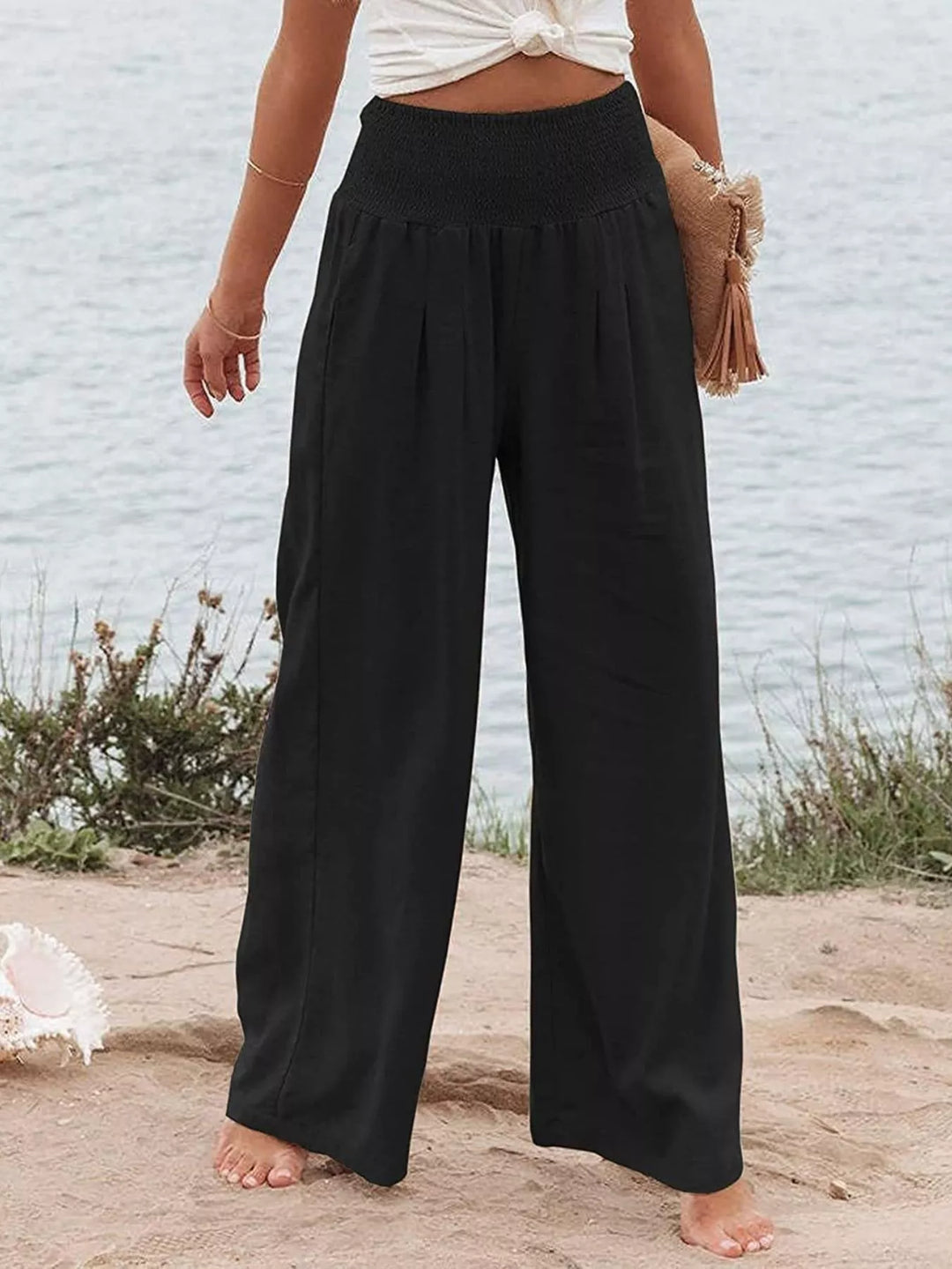 Black high waisted wide leg pants with smocked waist, front view on the beach
