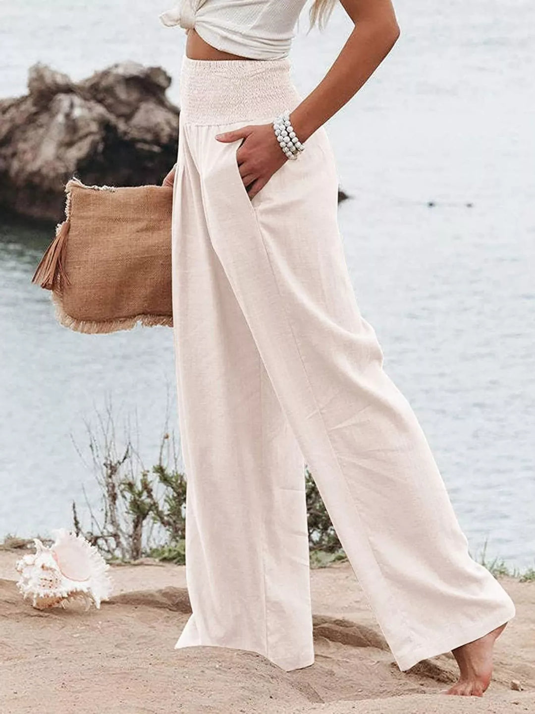 Women's high waisted wide leg pants in cream with smocked waist, beach setting