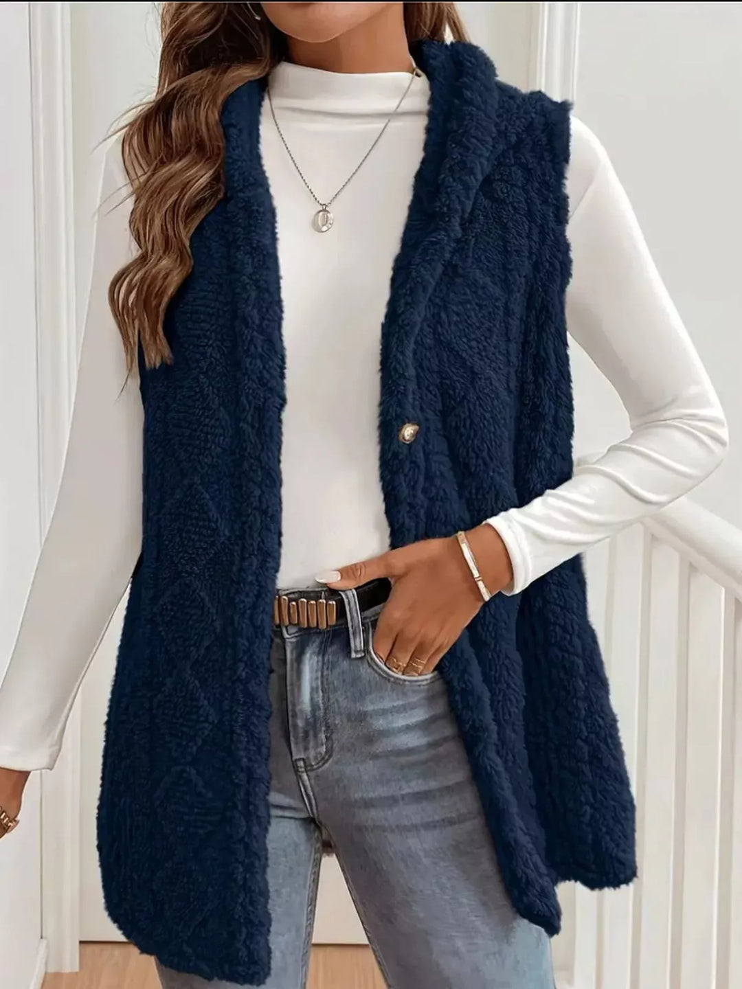 Navy hooded vest in cable knit, worn open with a white long sleeve top