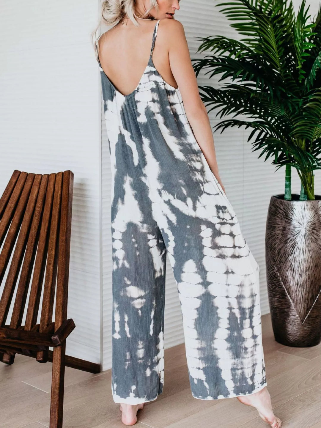 Gray tie dye jumpsuit back view, standing by a wooden chair