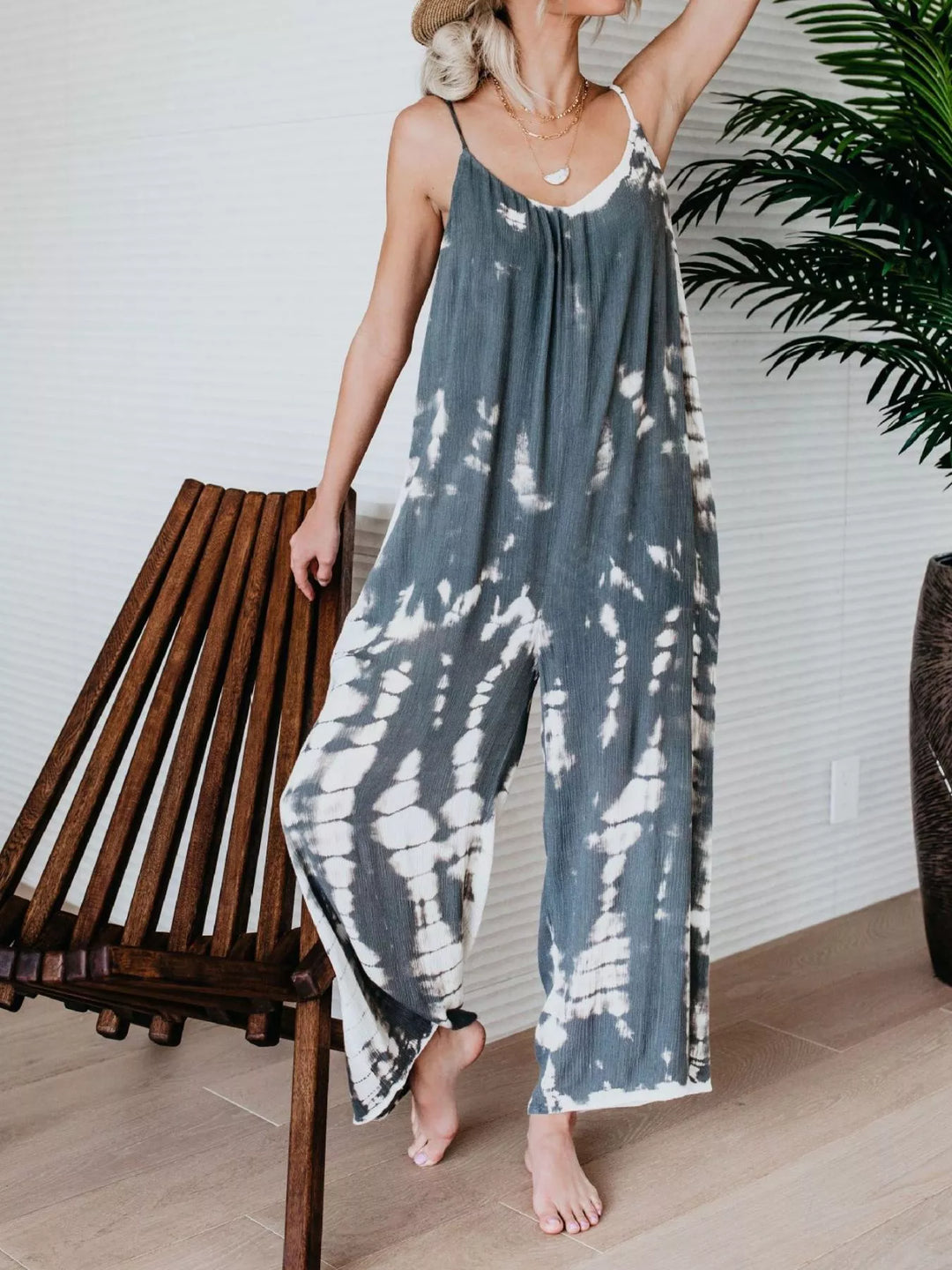 Gray tie dye jumpsuit with wide legs, hand on hip, beside a wooden chair