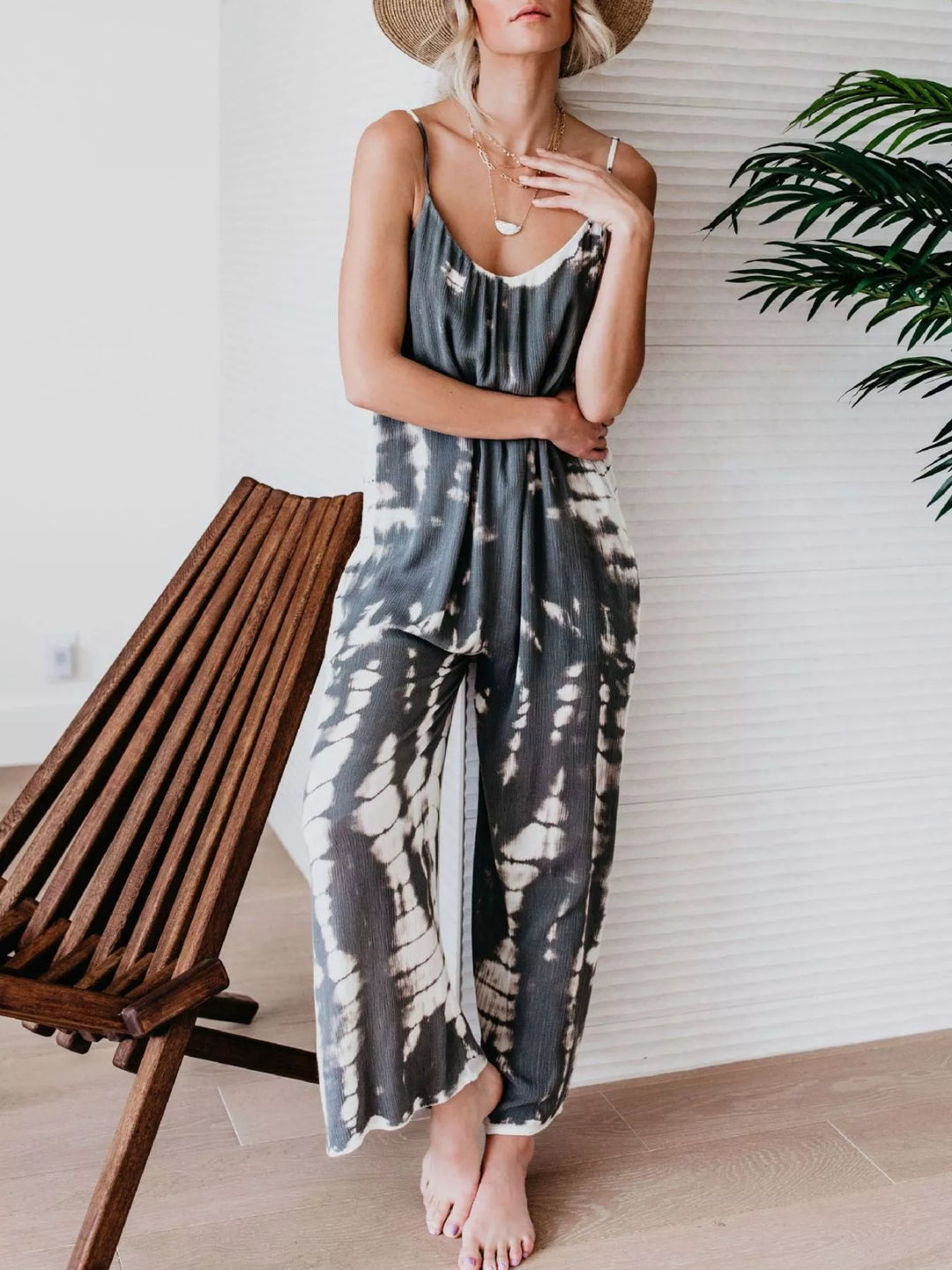 Gray tie dye wide leg jumpsuit, model standing near a palm plant